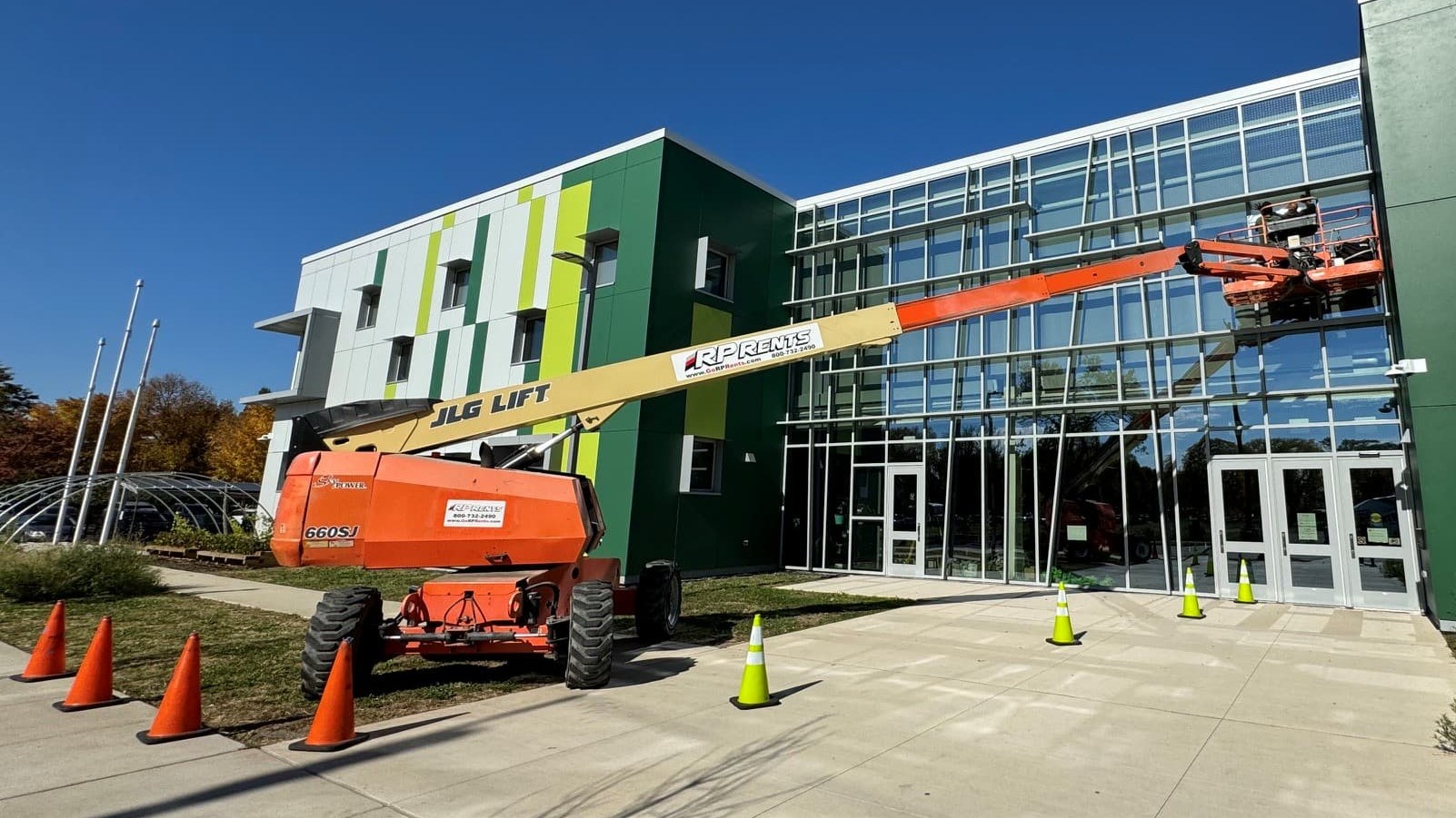 AAA Glass Tint installers working from a boom lift to apply bird strike window film on the glass curtain wall of a school, with the work area coned off.