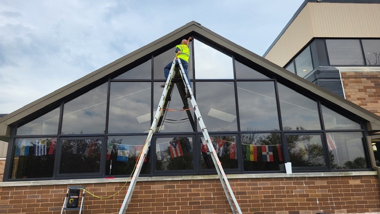 AAA Glass Tint installer applying exterior window film for glare reduction on a meeting space's triangular glass wall, which has a Low-E coating on surface 3.