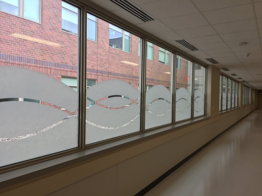 Hallway windows at Advocate Sherman Hospital in Elgin, Illinois, after AAA Glass Tint installed patterned decorative film with a custom cut flowing wave design along the lower glass.