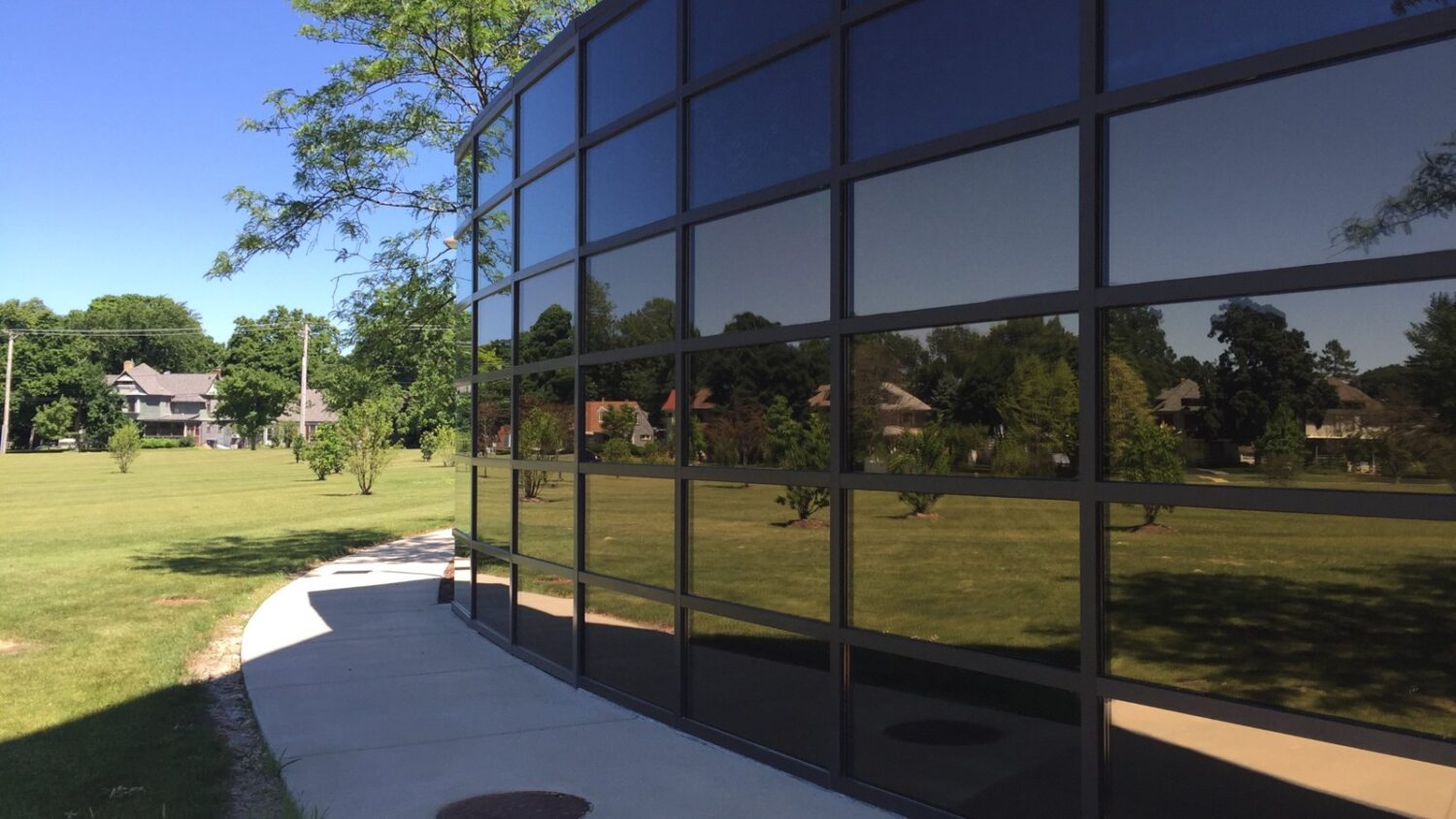 Curved glass curtain wall with reflective solar control window film installed by AAA Glass Tint, reflecting the lawn and trees outside.