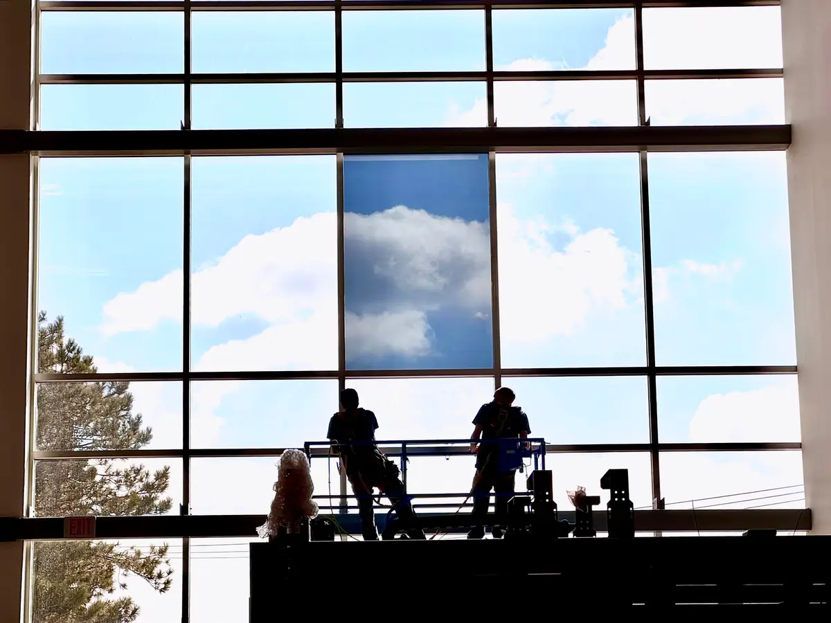 Two installers on a work platform inside a tall window wall, applying window film.