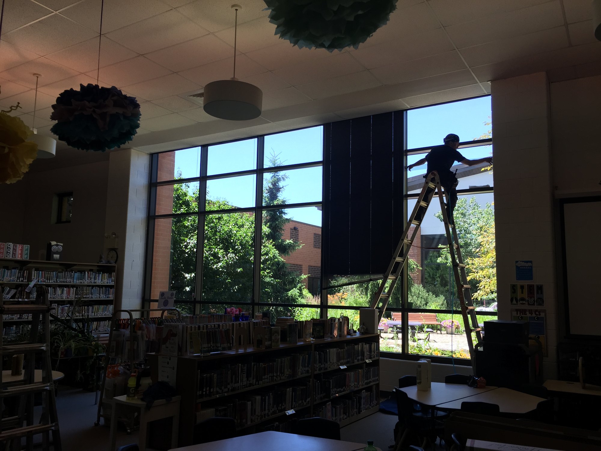 AAA Glass Tint installer on a ladder applying solar control window film to tall windows in a school library.